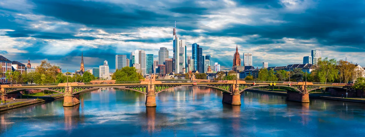 Die Frankfurter Skyline am Main mit dem Dom, im Vordergrund eine Brücke über den Fluss.